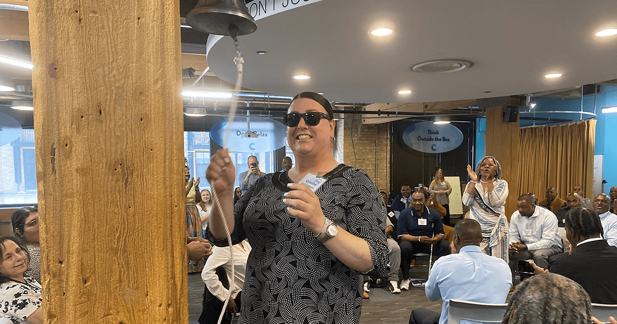 Photo of a woman wearing sunglasses ringing a bell to celebrate accepting her job offer.